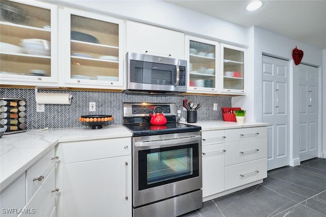 kitchen featuring backsplash, appliances with stainless steel finishes, white cabinets, glass insert cabinets, and light stone countertops