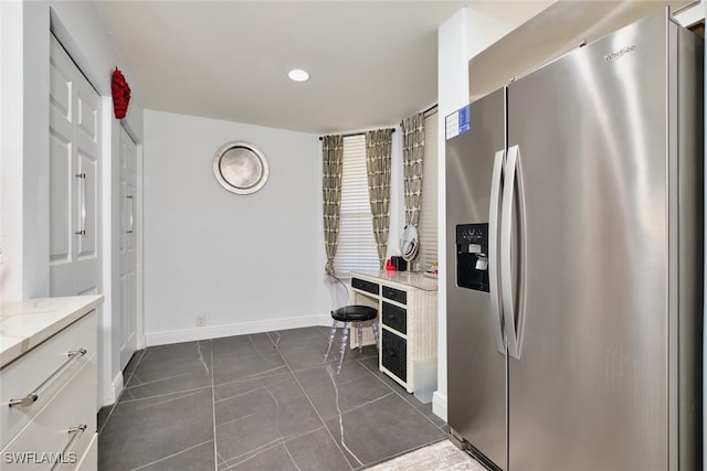 kitchen featuring baseboards, stainless steel fridge with ice dispenser, dark tile patterned floors, light stone counters, and white cabinetry