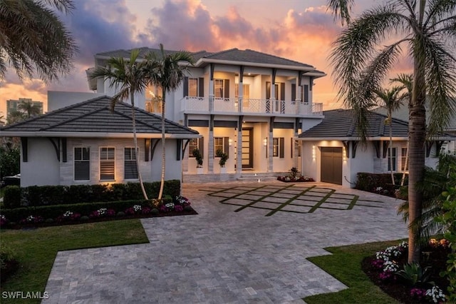 back of property featuring a tile roof, a balcony, decorative driveway, and stucco siding