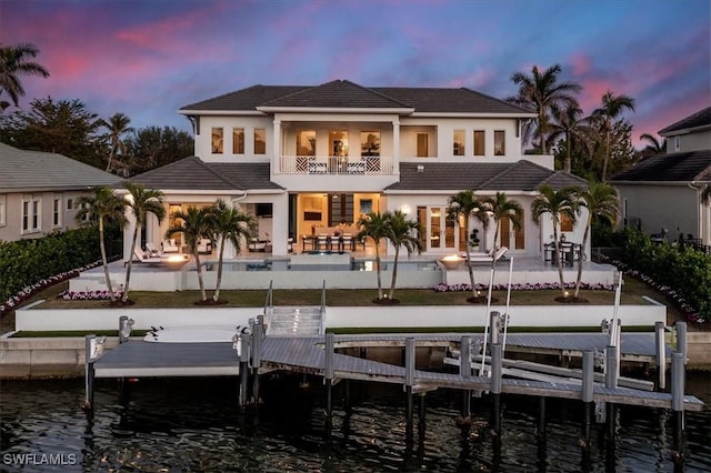 back of property at dusk featuring a patio area, boat lift, a tiled roof, and a balcony