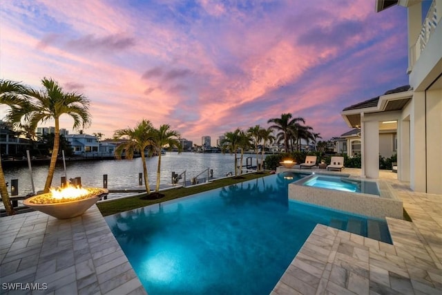 pool at dusk featuring a patio area, a fire pit, a water view, and a pool with connected hot tub