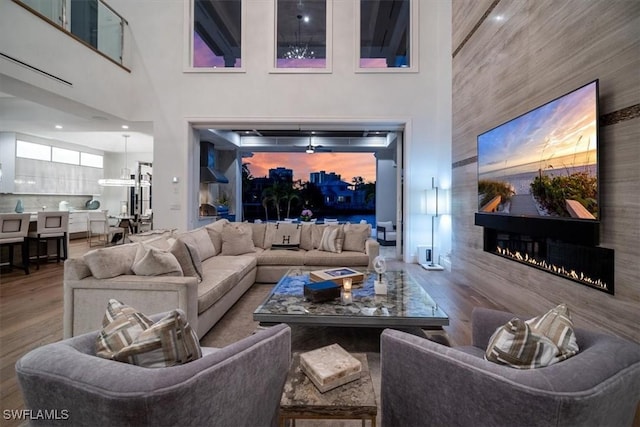 living area featuring a glass covered fireplace, a towering ceiling, and wood finished floors