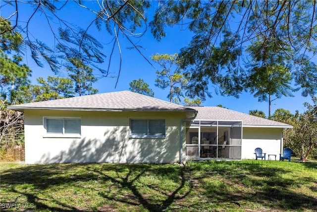 rear view of house featuring a shingled roof, a lawn, and stucco siding