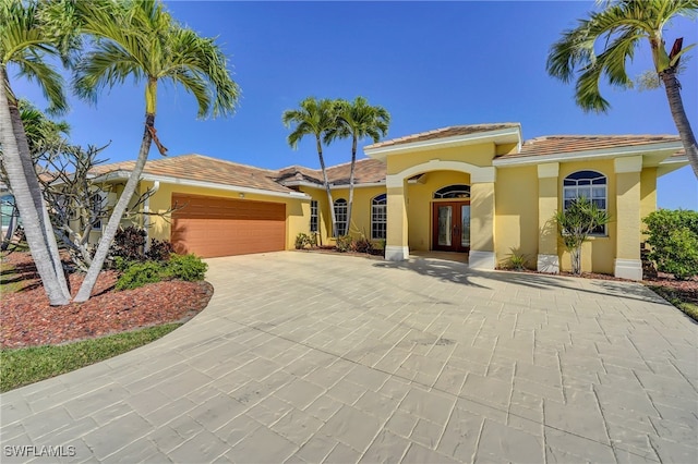 mediterranean / spanish house with a tiled roof, stucco siding, french doors, a garage, and driveway