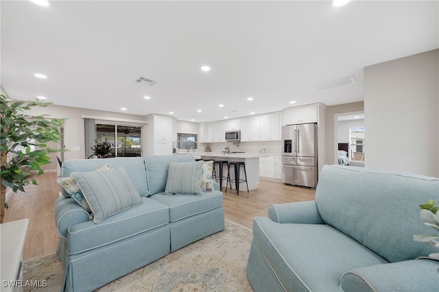 living room featuring light wood finished floors, visible vents, and recessed lighting