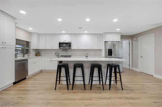 kitchen with light wood finished floors, a kitchen island, a sink, light countertops, and appliances with stainless steel finishes