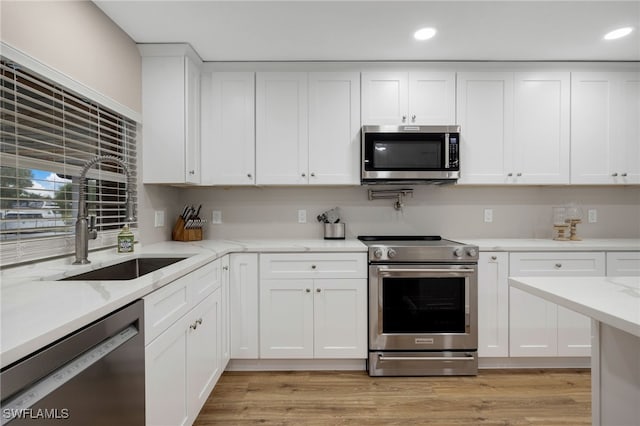 kitchen featuring light stone countertops, light wood-style flooring, a sink, stainless steel appliances, and white cabinets