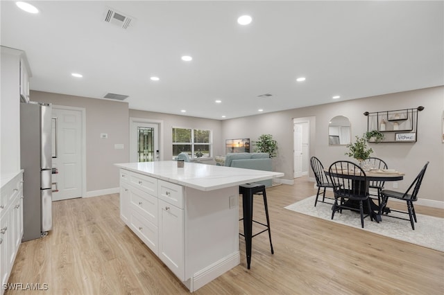 kitchen featuring light wood-type flooring, visible vents, white cabinetry, freestanding refrigerator, and arched walkways