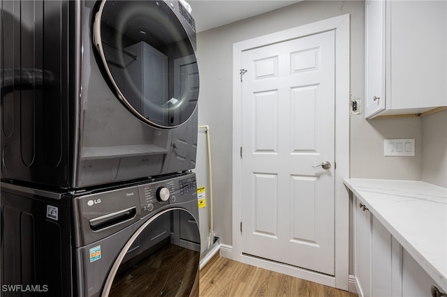 clothes washing area featuring cabinet space, light wood-style floors, and stacked washer / dryer