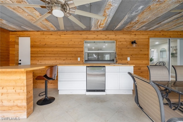 kitchen with ceiling fan, a sink, wood walls, white cabinetry, and stainless steel fridge