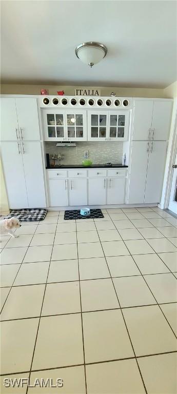 kitchen featuring light tile patterned floors, glass insert cabinets, backsplash, and white cabinetry