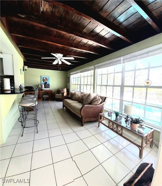 living area featuring tile patterned floors, beamed ceiling, wooden ceiling, and ceiling fan