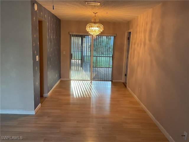 unfurnished dining area with a notable chandelier, wood finished floors, visible vents, and baseboards