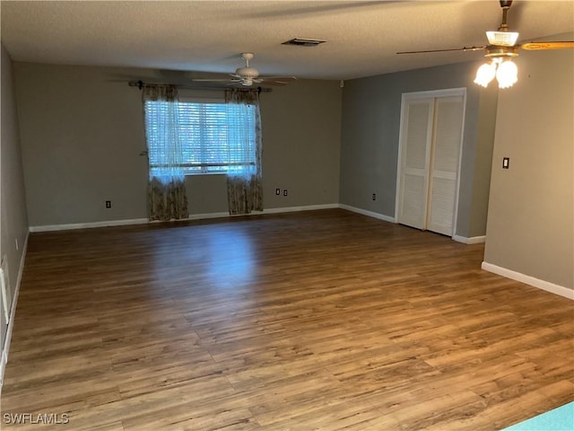 spare room with visible vents, a ceiling fan, a textured ceiling, wood finished floors, and baseboards