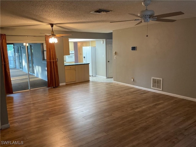 unfurnished living room featuring a ceiling fan, wood finished floors, visible vents, and a textured ceiling