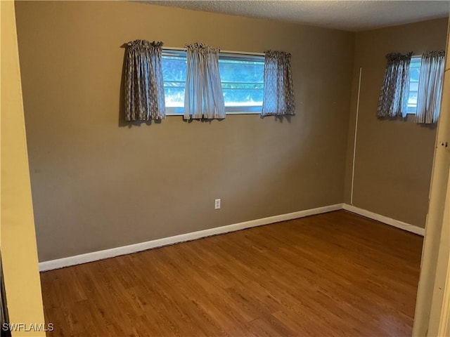 spare room featuring plenty of natural light, a textured ceiling, baseboards, and wood finished floors