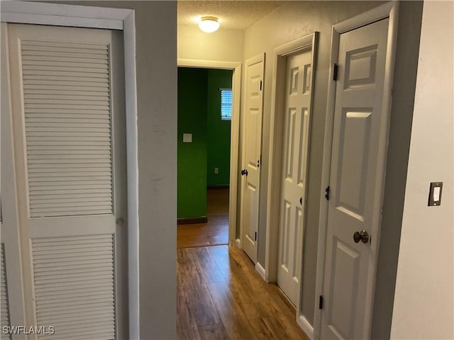 corridor with baseboards, dark wood-type flooring, and a textured ceiling