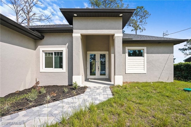 view of exterior entry with a yard, french doors, roof with shingles, and stucco siding