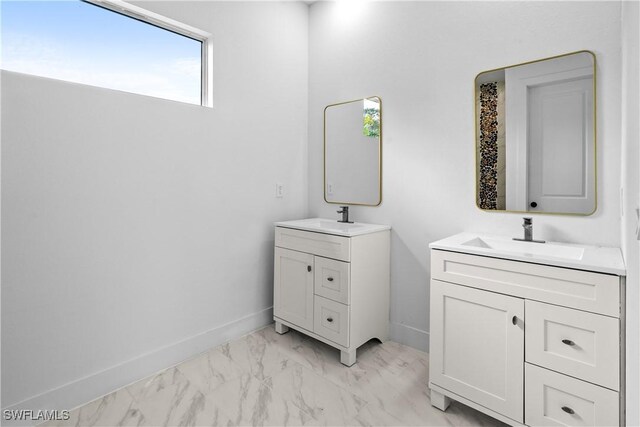 bathroom featuring marble finish floor, two vanities, baseboards, and a sink