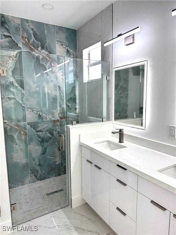 full bathroom with a marble finish shower, marble finish floor, double vanity, and a sink