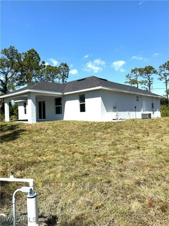 back of property featuring a yard, central AC unit, and stucco siding