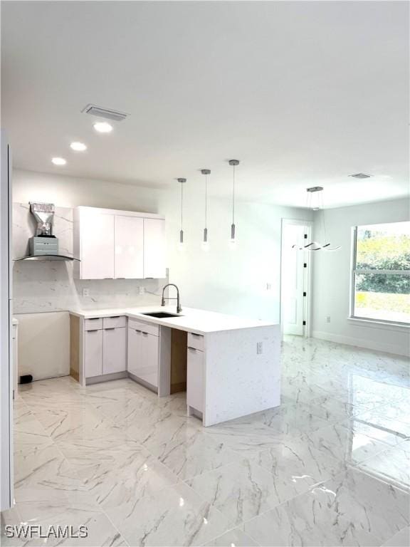 kitchen featuring a peninsula, pendant lighting, marble finish floor, and a sink