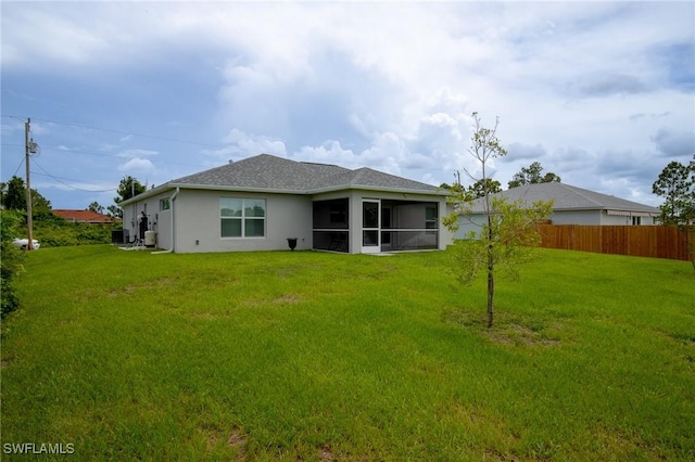 back of property featuring fence, central AC, stucco siding, a lawn, and a sunroom