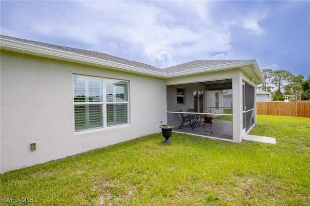 rear view of house featuring fence, roof with shingles, stucco siding, a yard, and a sunroom