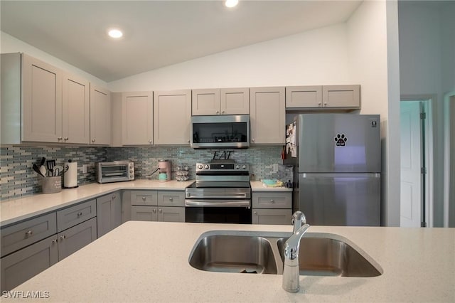 kitchen featuring lofted ceiling, a toaster, gray cabinets, a sink, and appliances with stainless steel finishes