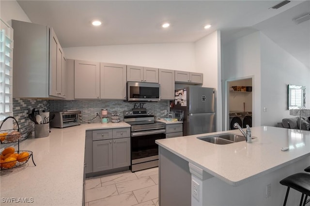 kitchen with washing machine and dryer, gray cabinetry, stainless steel appliances, and a sink