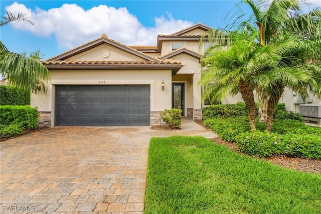 mediterranean / spanish-style home featuring decorative driveway, stone siding, an attached garage, and stucco siding