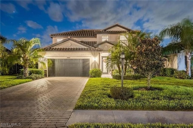 mediterranean / spanish-style house featuring stucco siding, a front lawn, a garage, a tiled roof, and decorative driveway