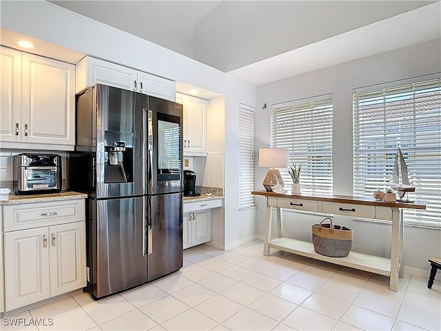 kitchen featuring light tile patterned floors, baseboards, tasteful backsplash, and black fridge with ice dispenser