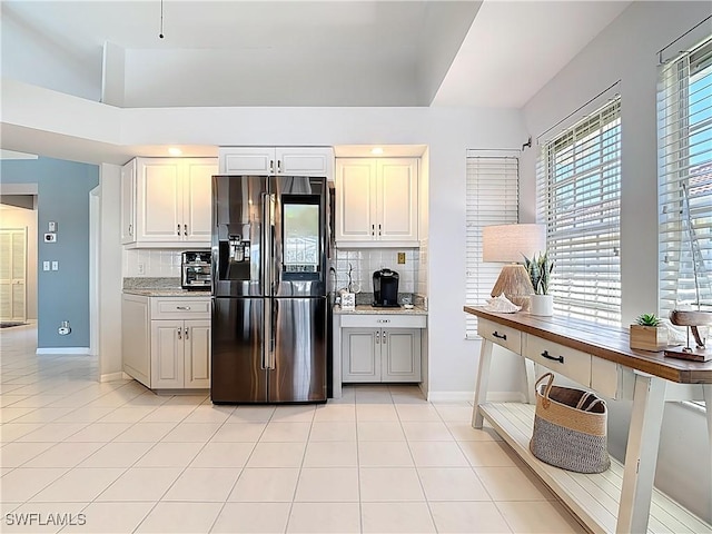 kitchen featuring fridge with ice dispenser, light stone counters, light tile patterned floors, decorative backsplash, and baseboards