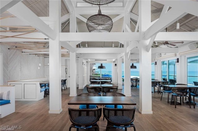 dining room featuring ceiling fan with notable chandelier, beamed ceiling, wood finished floors, and a towering ceiling