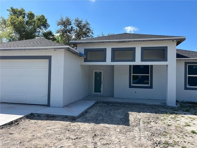 view of front of house with stucco siding, an attached garage, and a shingled roof