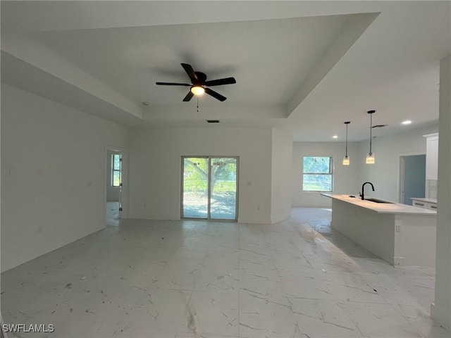 unfurnished living room featuring a sink, a tray ceiling, marble finish floor, and ceiling fan