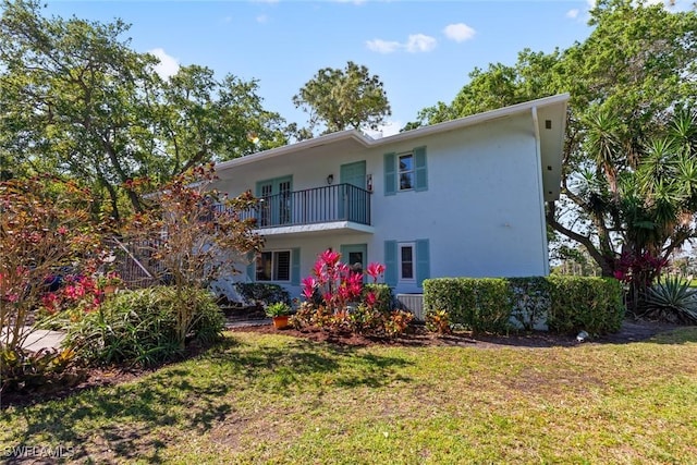 rear view of house with a balcony, a yard, and stucco siding