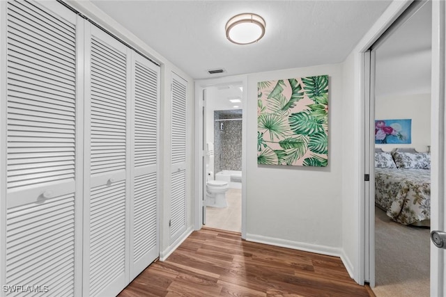 corridor featuring visible vents, baseboards, and wood finished floors