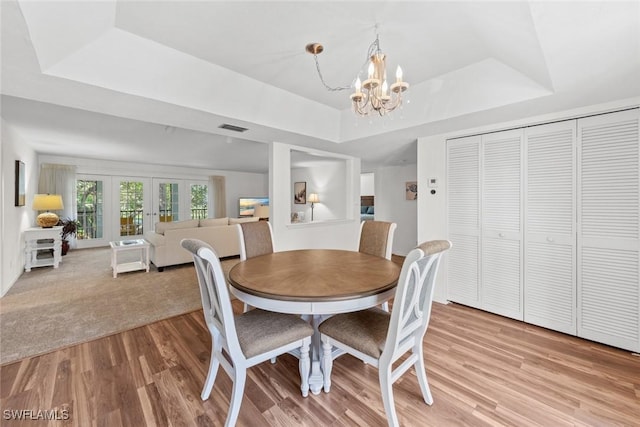 dining area featuring light wood finished floors, visible vents, a chandelier, and a raised ceiling