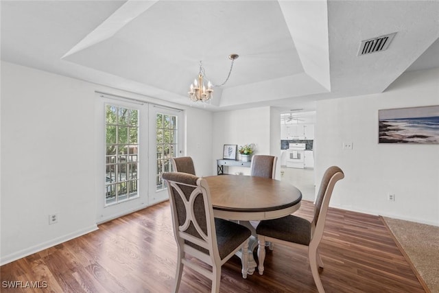 dining room with a raised ceiling, wood finished floors, visible vents, and baseboards