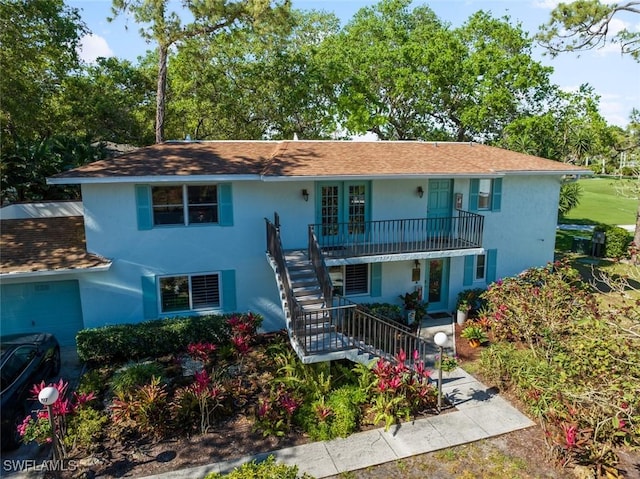 view of front of property with stairway, an attached garage, covered porch, and stucco siding