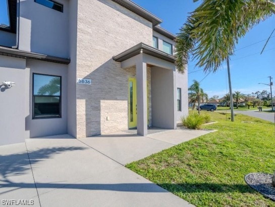 doorway to property with a patio area, stucco siding, and a lawn