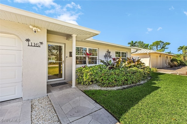 property entrance featuring stucco siding, a yard, and an attached garage