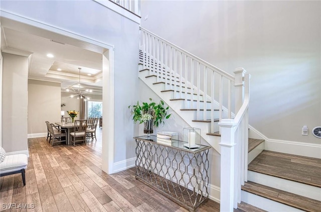 stairs with ornamental molding, a tray ceiling, wood finished floors, an inviting chandelier, and baseboards