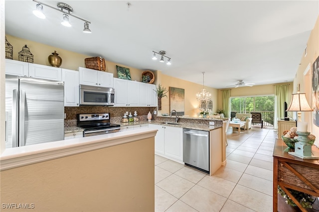 kitchen with light tile patterned floors, a peninsula, a sink, stainless steel appliances, and backsplash