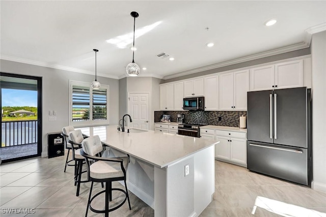 kitchen with an island with sink, a sink, backsplash, stainless steel appliances, and white cabinets