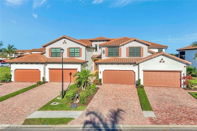 mediterranean / spanish-style house with a tile roof, decorative driveway, a garage, and stucco siding