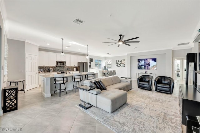 living area featuring crown molding, light tile patterned flooring, a ceiling fan, and visible vents