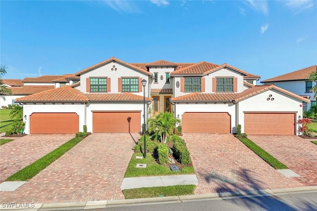 mediterranean / spanish home featuring stucco siding, a tiled roof, and decorative driveway